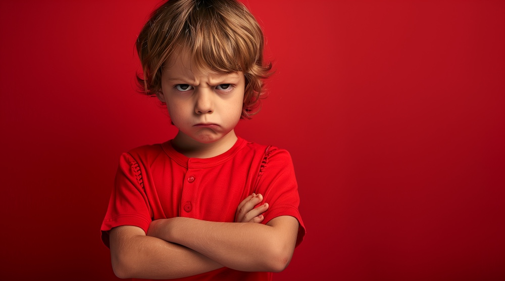 studio portrait of a very angry and petulant child in a red shirt. arms folded. exaggerating and feigning anger