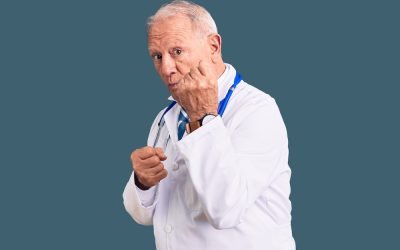 senior handsome grey haired man wearing doctor coat and stethoscope ready to fight with fist defense gesture, angry and upset face, afraid of problem